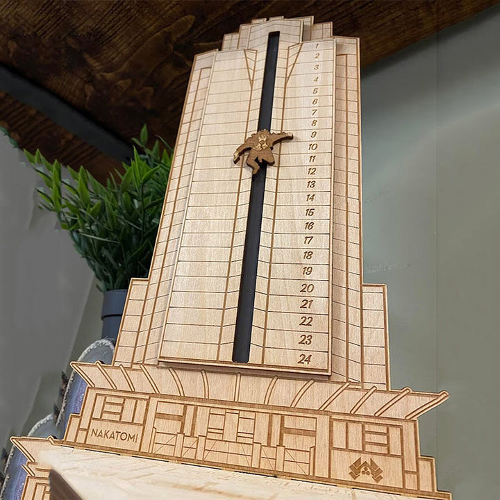 "Detaljerad trä Adventskalender med Die Hard-motiv, visar Hans Gruber faller från brunblå Nakatomi Plaza, roterbar design."